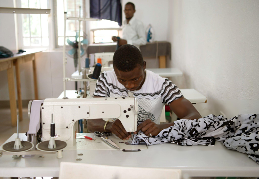 A Nigerian tailor at work in his workshop, sewing traditional Ankara fabric — representing the artisan economy behind African fashion